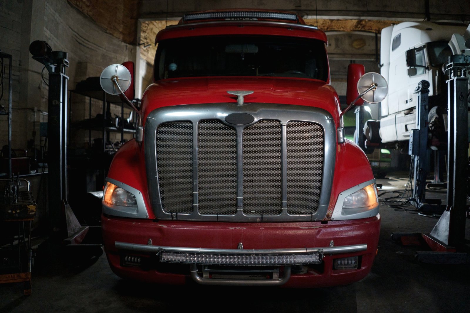 A tractor unit parked nose-on in a repair bay with its lights on
