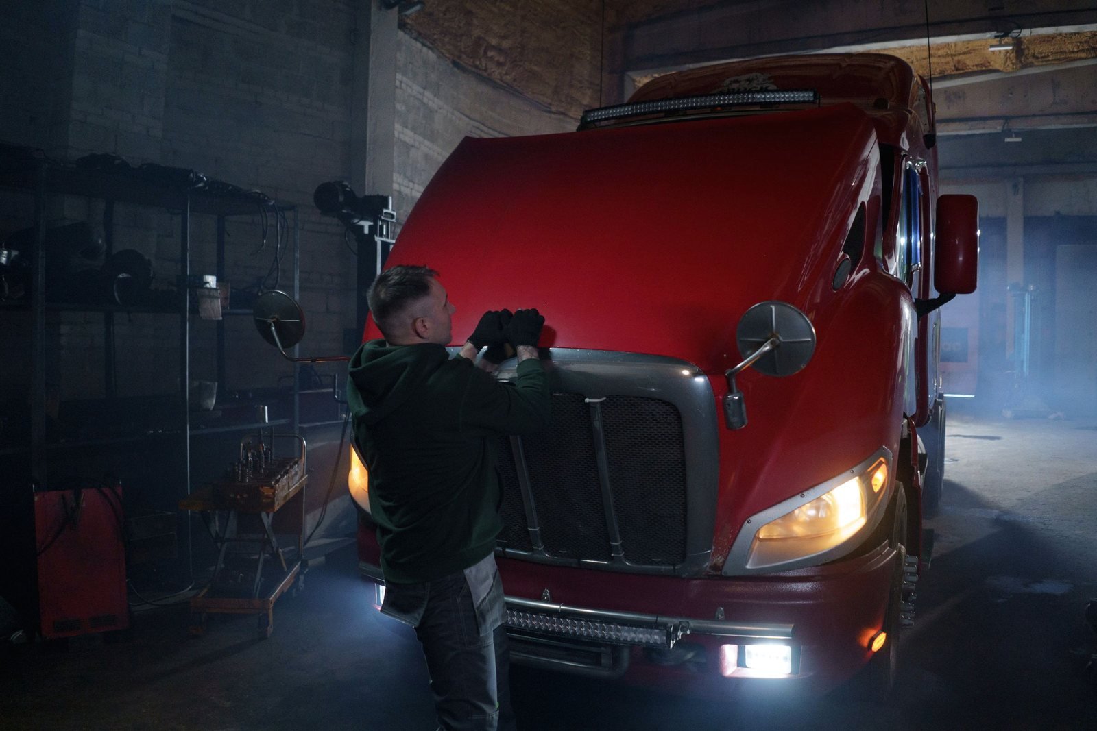 A technician at the open hood of a tractor unit in a service bay